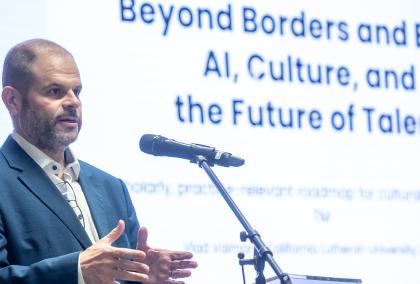 Vlad Vaiman giving a presentation, with a title slide behind him saying "Beyond borders and bias: AI, Culture, and the Future of Talent"
