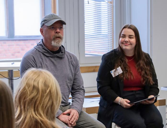 Jamie Hyneman and Jenni Halonen sitting on chairs in front of a class room, talking to people in the room