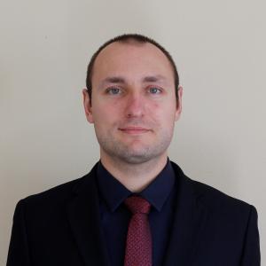 Person with a shaved head, black shirt and red tie looking at the camera