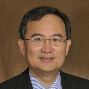 Person with short black hair and black suit smiling at the camera